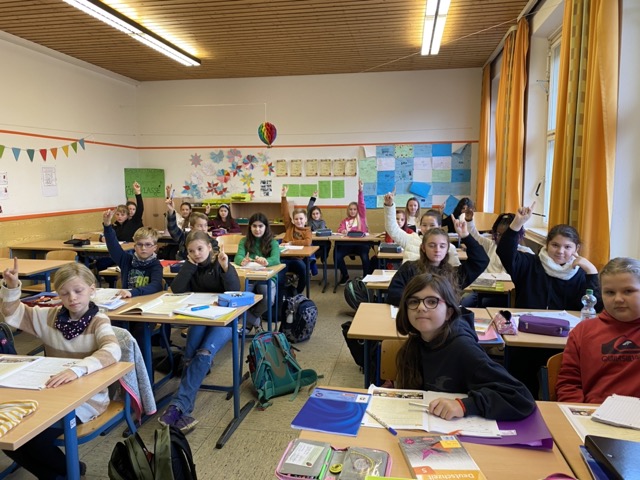 Kinder in Klassenzimmer mit teilweise gehobenen Händen